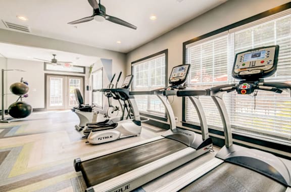A row of treadmills in a gym with a fan and windows at The Hartley at Sweetwater Creek, Duluth, Georgia