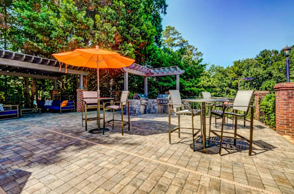 A patio with a table and chairs under an orange umbrella at The Hartley at Sweetwater Creek, Duluth, Georgia 30096