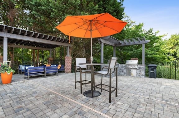 A patio with a table, chairs and an orange umbrella at The Hartley at Sweetwater Creek, Duluth, 30096
