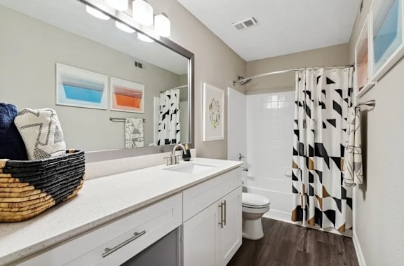 A bathroom with a white countertop and a black and white shower curtain with a garden style tub at The Hartley at Sweetwater Creek, Duluth, GA.
