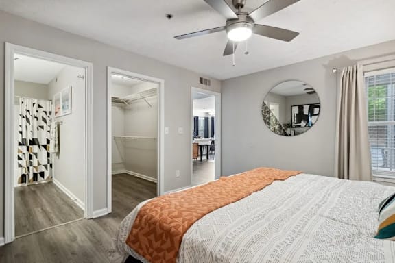 A bedroom with a bed, a ceiling fan, and a mirror on the wall with a view of the large closet at The Hartley at Sweetwater Creek, Duluth, Georgia 30096