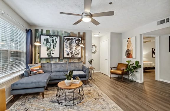 A living room with a grey sofa, a coffee table, and a ceiling fan at The Hartley at Sweetwater Creek, Duluth, GA