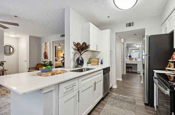 A modern kitchen with white cabinets and a black refrigerator with a breakfast bar at The Hartley at Sweetwater Creek, Duluth, GA