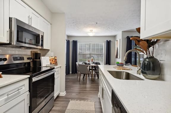 A kitchen with white cabinets and a black stove top oven at The Hartley at Sweetwater Creek, Duluth 30096