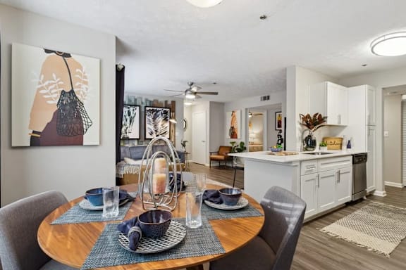A dining room with a table set for two and a painting on the wall with a view of the kitchen with a breakfast bar at The Hartley at Sweetwater Creek, Duluth, Georgia