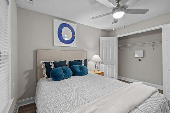 A bedroom with a bed, pillows, a ceiling fan, and a mirror.