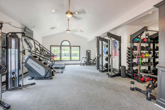 A spacious gym with a variety of equipment including treadmills, weights, and a ceiling fan.