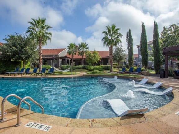 a large swimming pool with chairs and palm trees