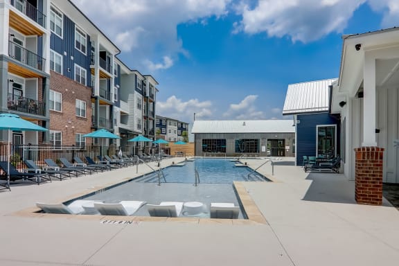 a swimming pool with lounge chairs and umbrellas in front of an apartment building
