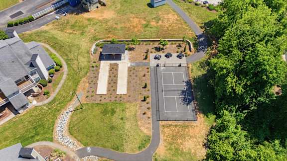 A tennis court is surrounded by a grassy area and a few trees.