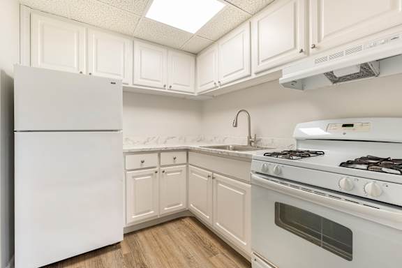A white kitchen with a refrigerator, stove, and cabinets.