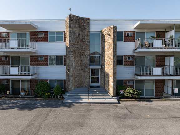 A stone pillar stands in front of a white building with balconies.