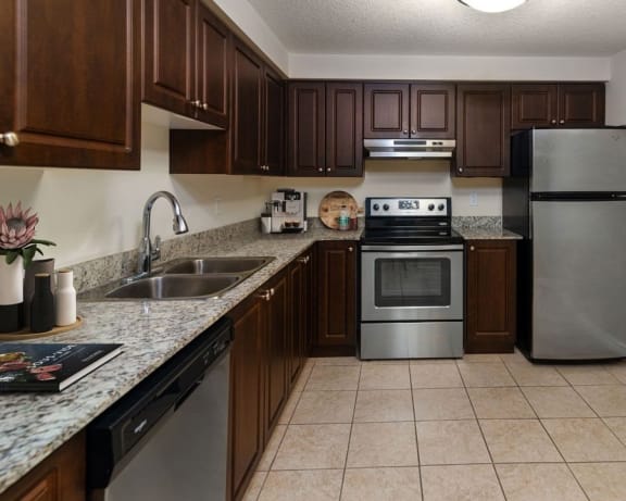 L-shaped kitchen with dark wood cabinets, refrigerator, and dishwasher.