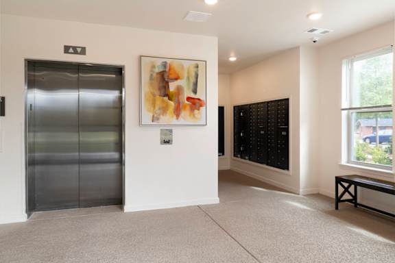 A hallway with a bench, a painting, and a wall of lockers.