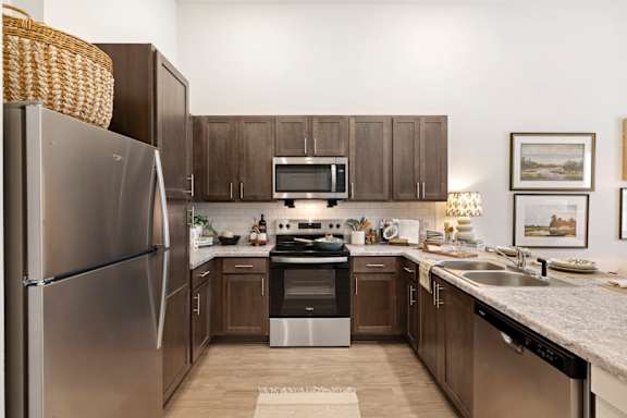 A kitchen with a refrigerator, microwave, oven, sink, and cabinets.