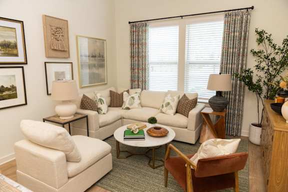 A living room with a white couch, a brown chair, and a coffee table with a green book and a plate of cookies on it.