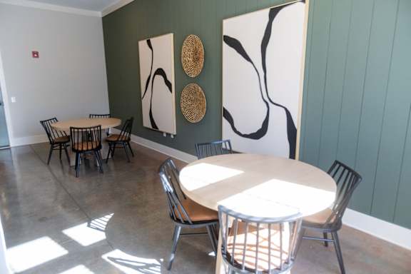 A room with a white table and chairs and a wall with a large painting and three woven baskets.