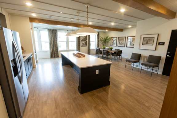 A kitchen with a refrigerator on the left and a dining table with chairs in the middle of the room.