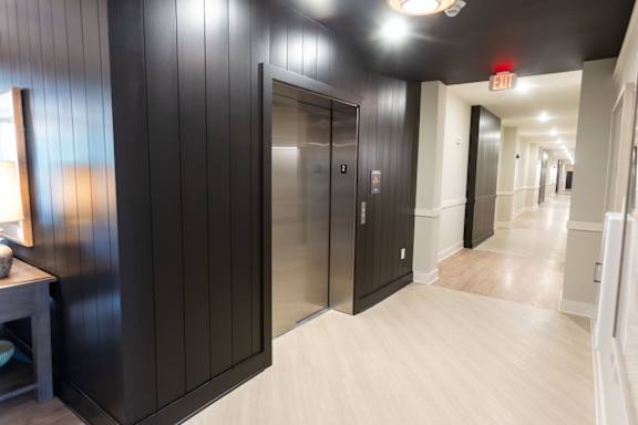 A long hallway with a black wall and a silver elevator.