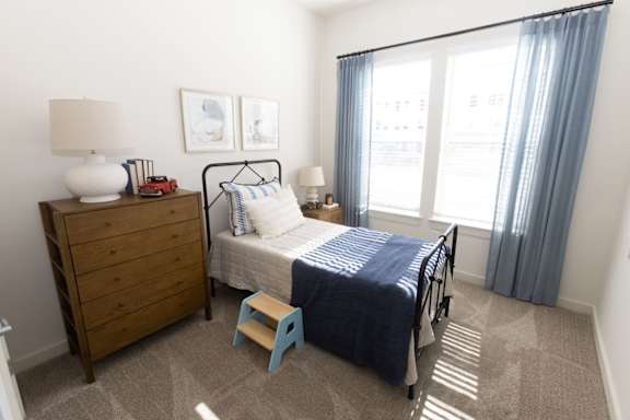 A bedroom with a bed, a nightstand, a lamp, and a chair.
