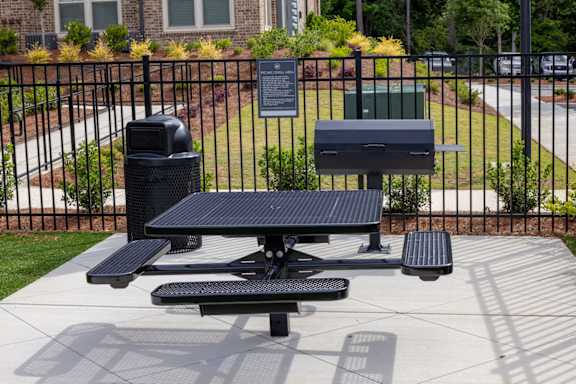 A black picnic table with a trash can and a recycling bin in front of a black fence.