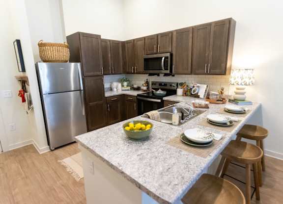 A kitchen with a refrigerator, microwave, oven, and a counter with plates and bowls on it.