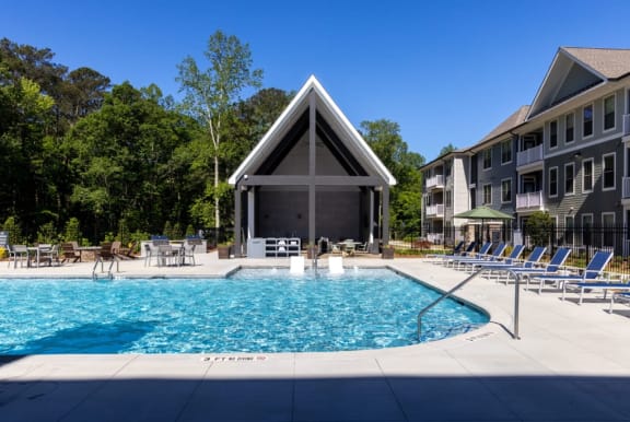 a swimming pool with lounge chairs and umbrellas in front of a gray building with a at Walton Fayetteville, Georgia, 30214