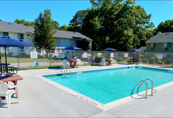 a swimming pool with chairs and umbrellas in front of houses at Brookwood at Ridge, New York, 11961