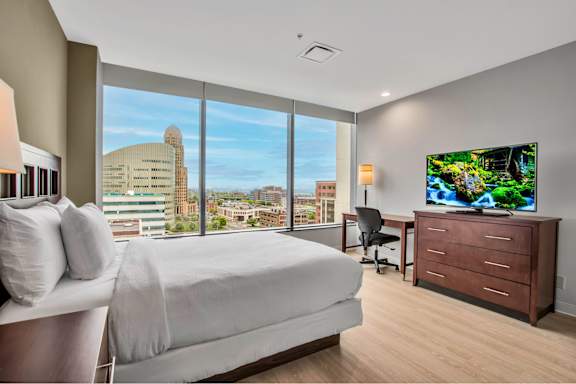 A bedroom with a large bed, a desk with a chair, and a flat-screen TV displaying a nature scene.