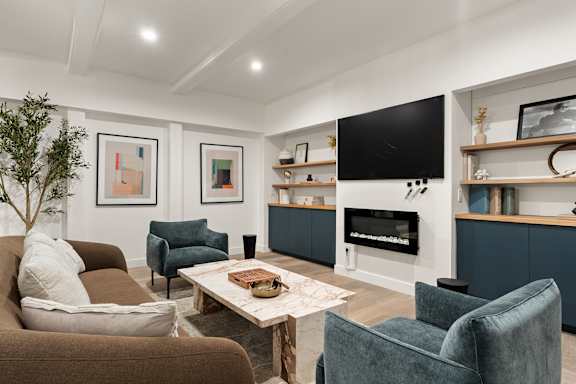 A living room with a brown couch, a blue chair, a coffee table, and a flat screen TV mounted on the wall.