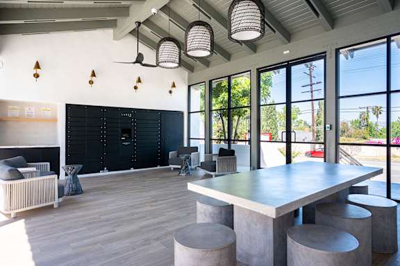 A room with a long table and chairs with a black wall and windows.
