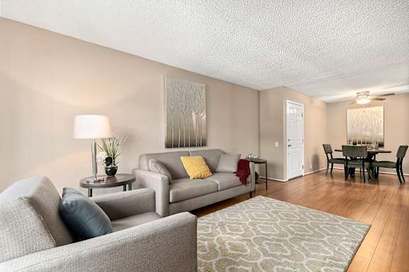 A living room with a grey couch, a grey armchair, a grey coffee table, a grey rug, a white door, a white cabinet, a white wall, a white ceiling, a white floor, a white lamp, a