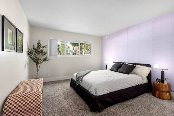 A bedroom with a bed, a small tree, and a lamp.
