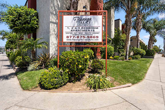 A sign for Topanga Terrace Apartments is displayed in front of a building.