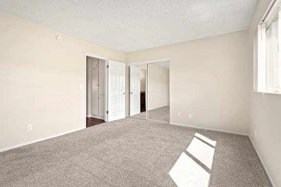 A room with carpeted floor and white walls with a doorway leading to another room.
