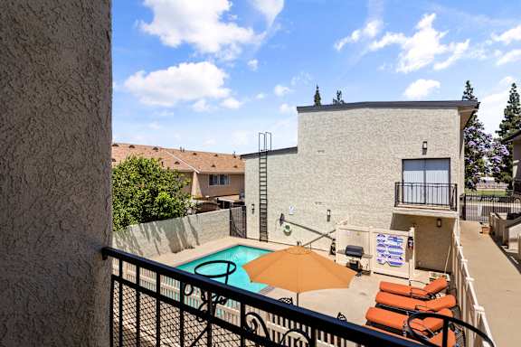 A pool with chairs and an umbrella is surrounded by a fence.