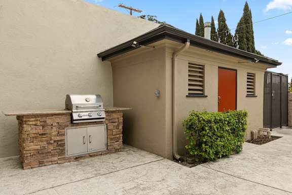 A small house with a red door and a BBQ grill on a stone base.