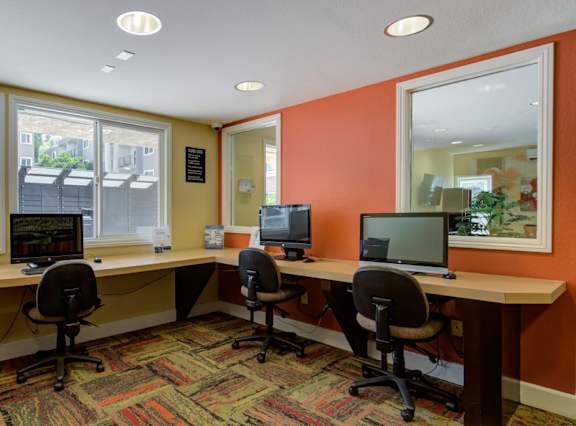 A room with orange walls has a desk with two chairs and two computers on it.