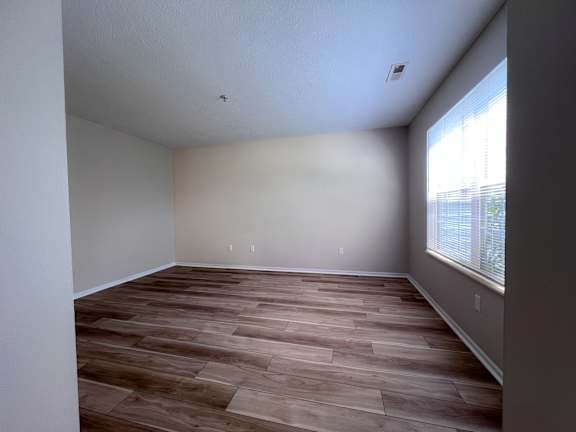 A room with wooden flooring and a window on the right side.