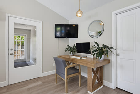 A room with a desk and a chair with a mirror and a television on the wall.
