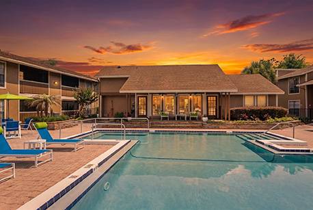 A swimming pool in front of a house with a sunset in the background.