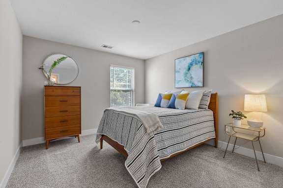 A bedroom with a bed, nightstand, and a plant on a dresser.