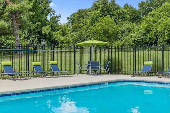 A pool surrounded by a black fence with a green umbrella and chairs.