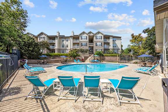A pool surrounded by chairs in front of apartment buildings.