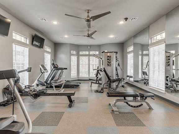 A spacious gym with a variety of equipment and a ceiling fan.