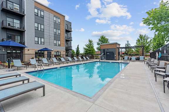 A swimming pool surrounded by lounge chairs and umbrellas in front of a modern apartment building.