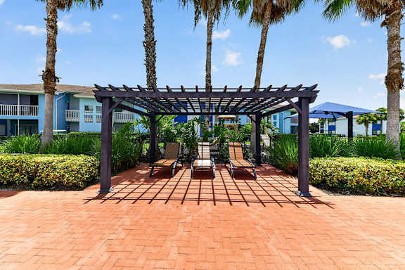 A patio with a pergola and chairs.