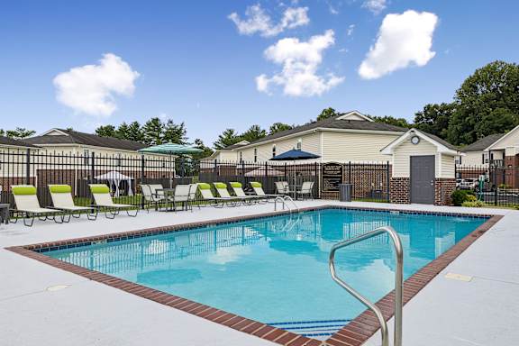 A large swimming pool surrounded by a fence and lounge chairs.