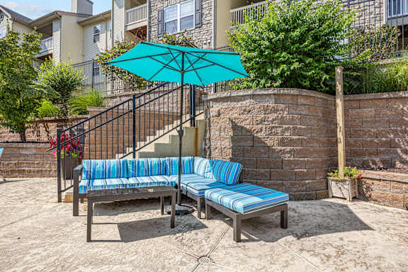A blue and white striped bench sits under a blue umbrella on a patio.