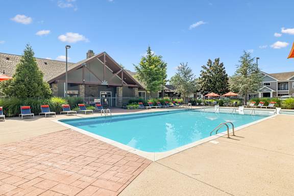 A large swimming pool surrounded by a brick patio and lounge chairs.